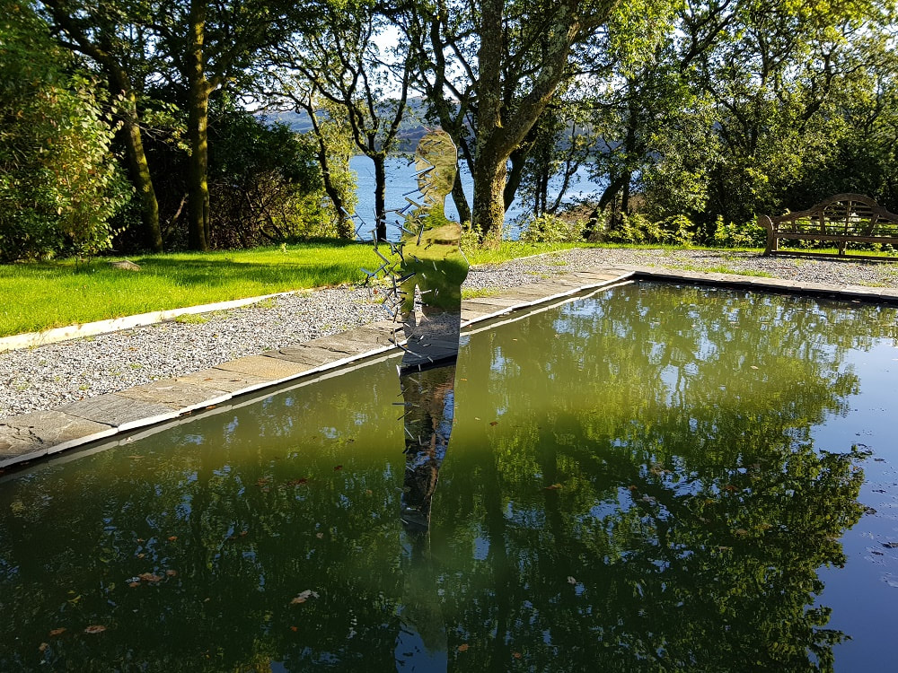 A mirrored sculpture of a female figure standing in a pool of water