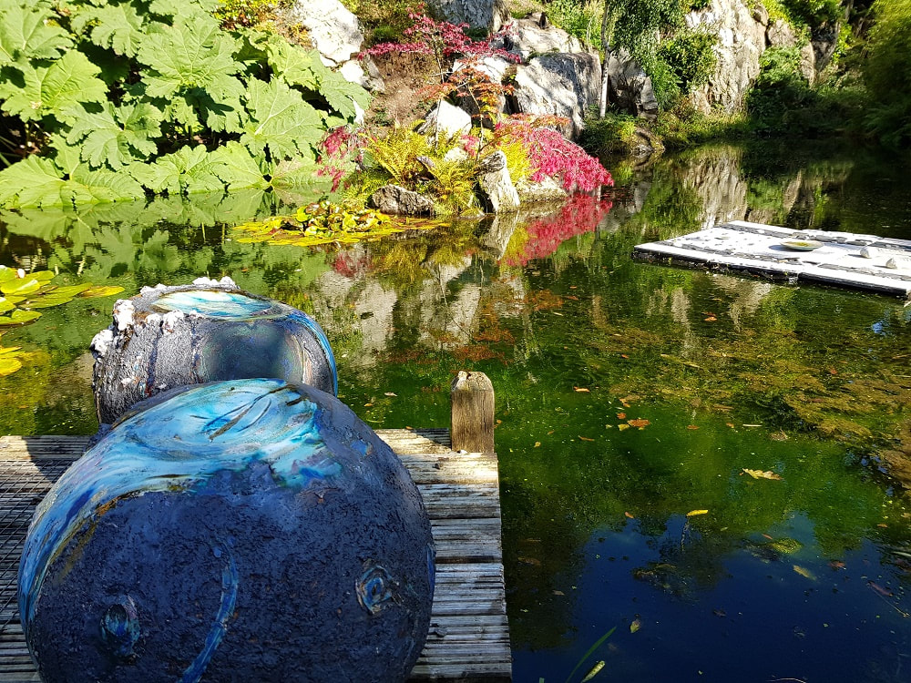 A pond surrounded by shrubbery with two blu e ball sculptures in the foreground