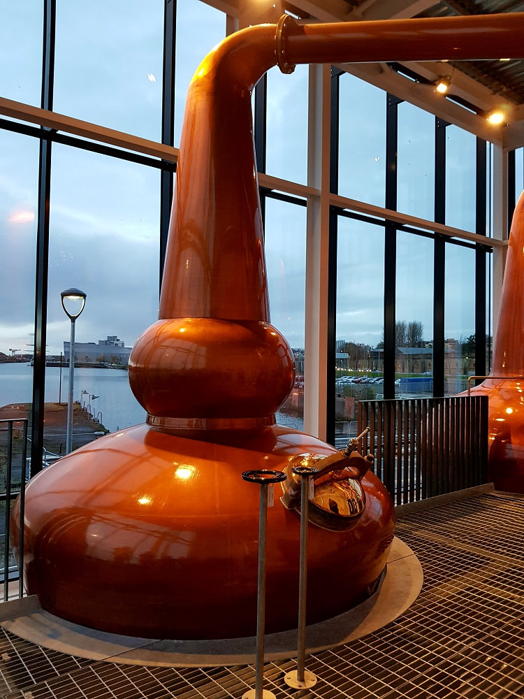 2 copper whisky stills with a view of the River Clyde behind