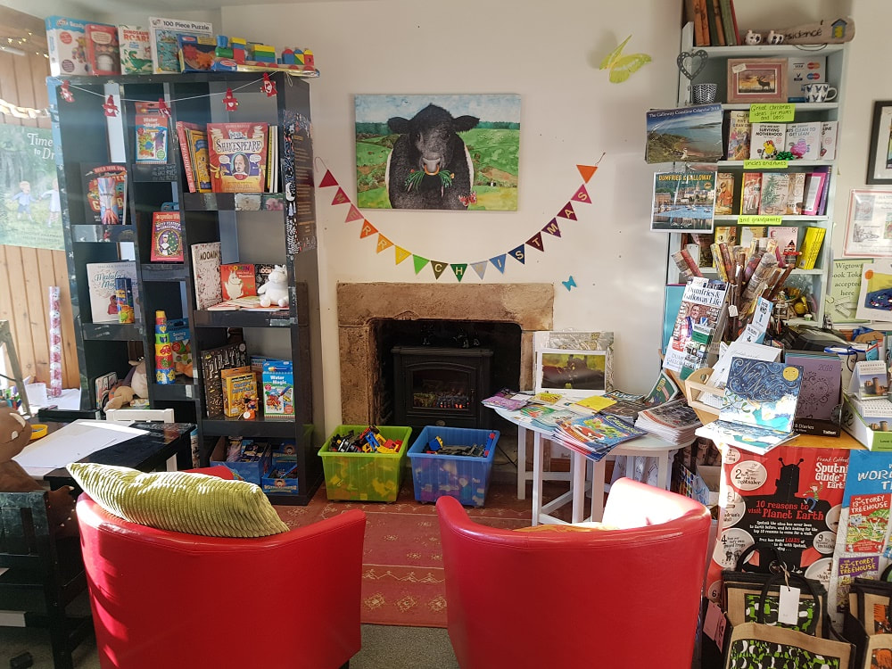The interior of a bookshop with shelves of children's books and two small red chairs