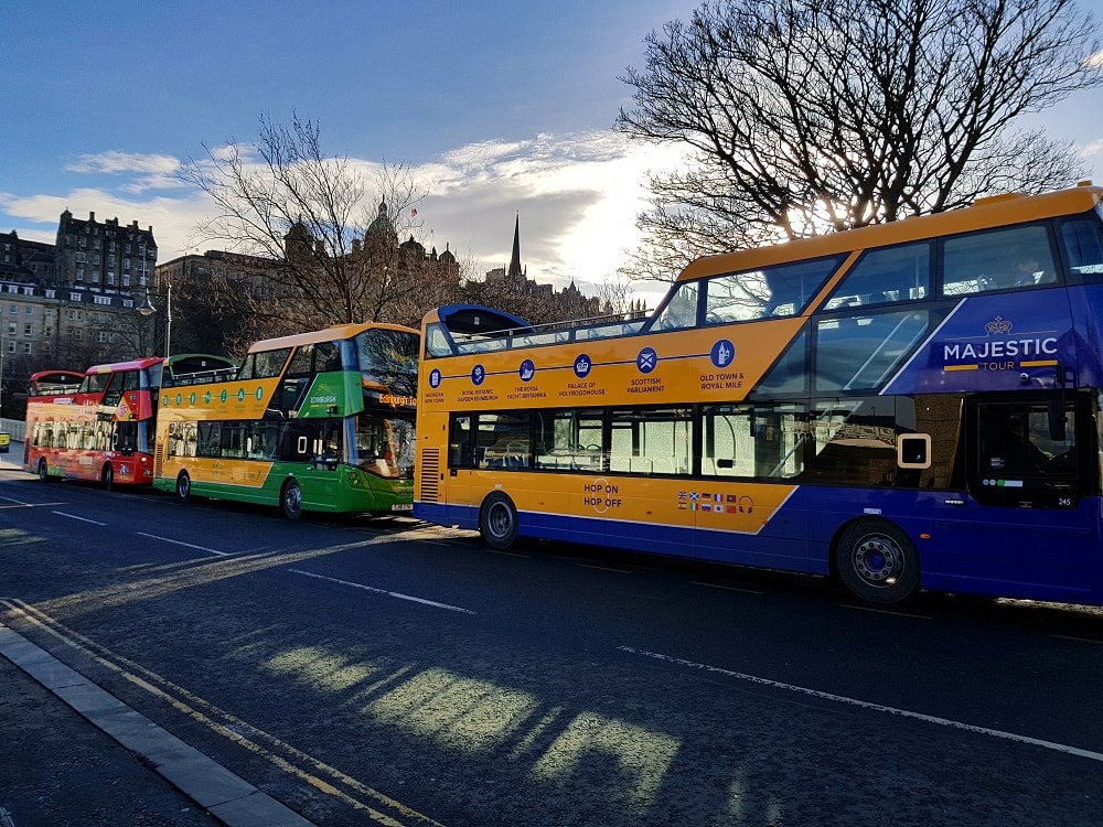 Three open top tour buses stopped at a bus stop