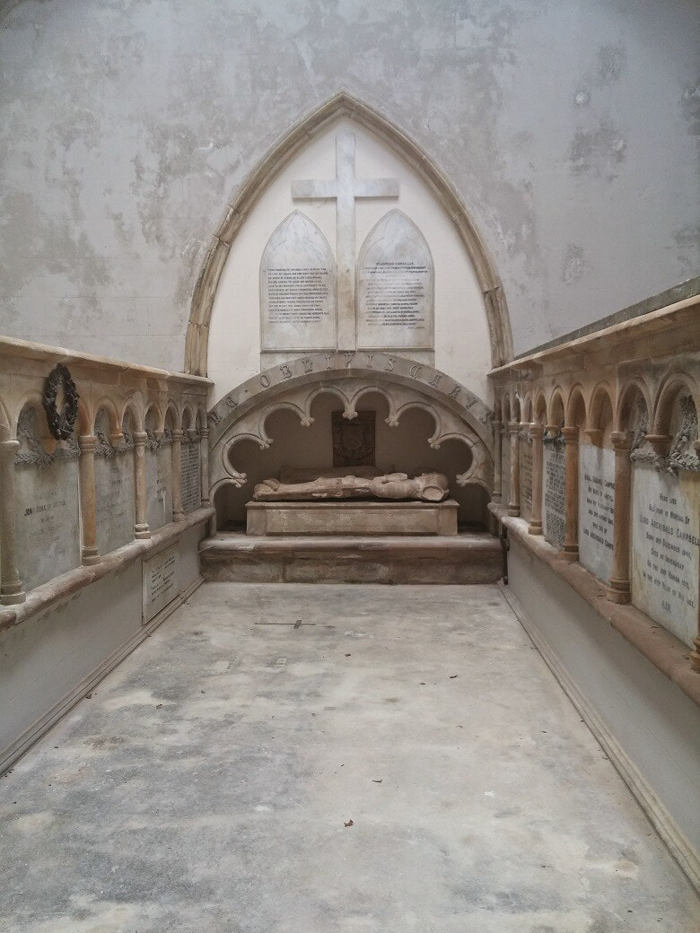 A white marble mausoleum with a carved effigy in the background and memorial stones on either side