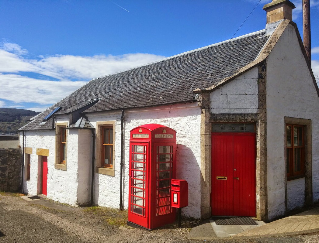 A white cottage with a red door and a red telephone box and post box outside