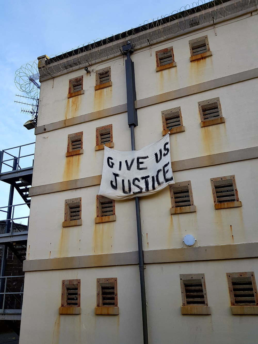 A beige building with a white banner hanging from one window reading ' Give us justice'