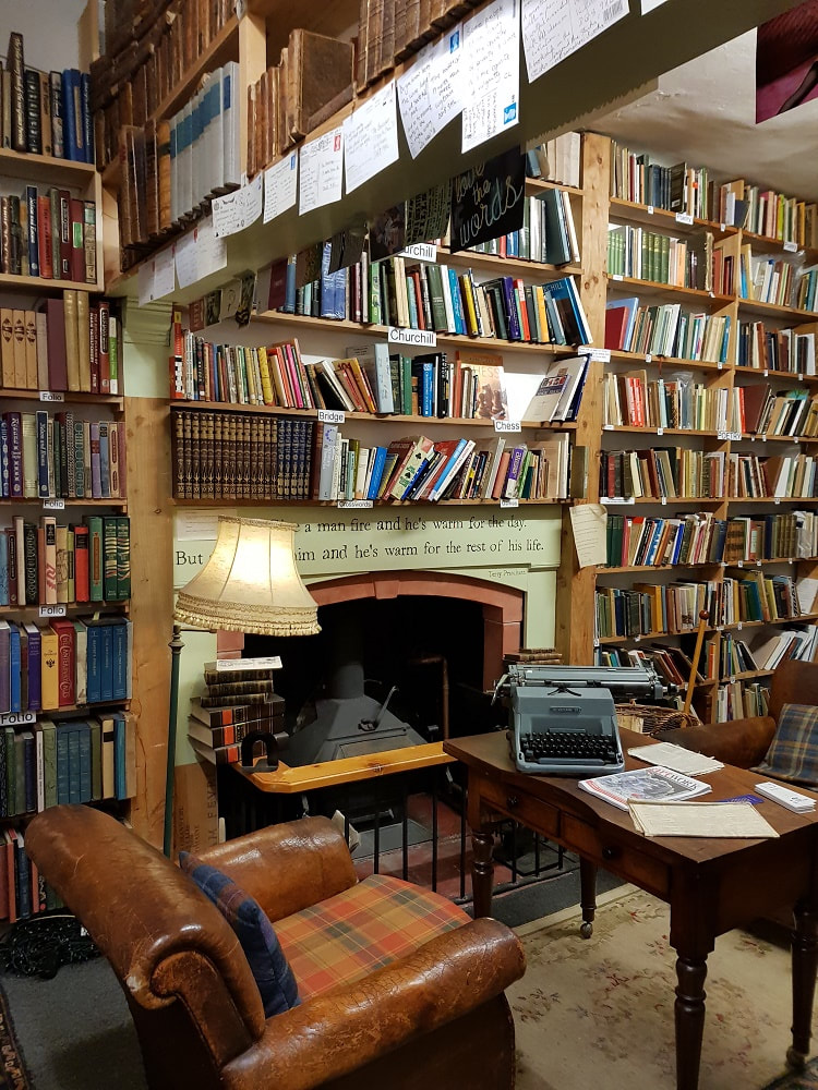 A room with rows of shelves filled with books, a leather armchair and a wooden table with a typewriter on top
