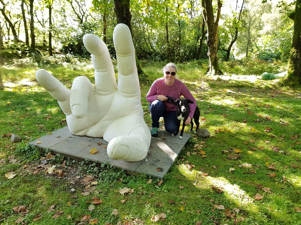 A woman and a black dog standing next to the sculpture of a large white hand