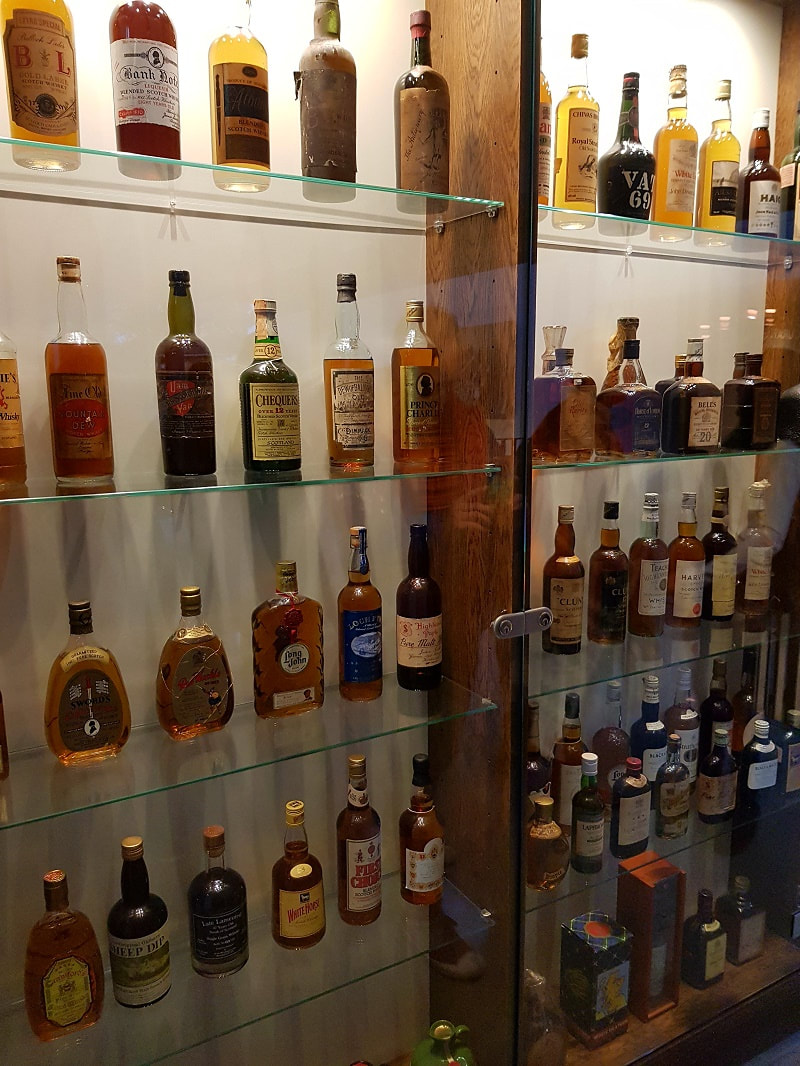 A glass display cabinet with 5 shelves filled with whisky bottles