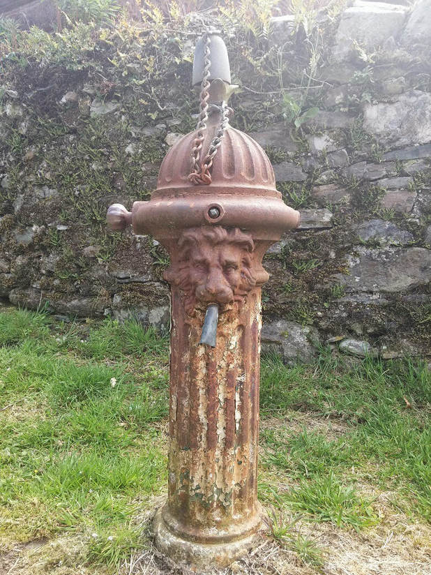 A brown metal water fountain with a lions head