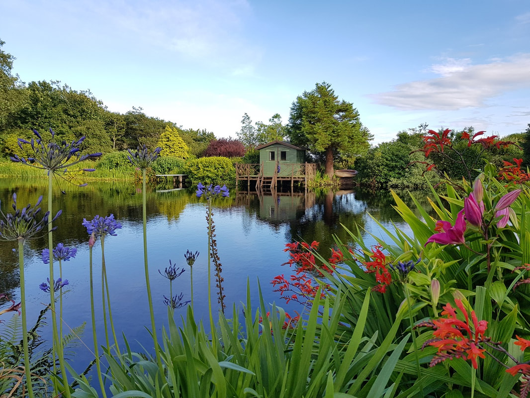 A lake surrounded by brightly coloured flowers with a green boating hut on the far side