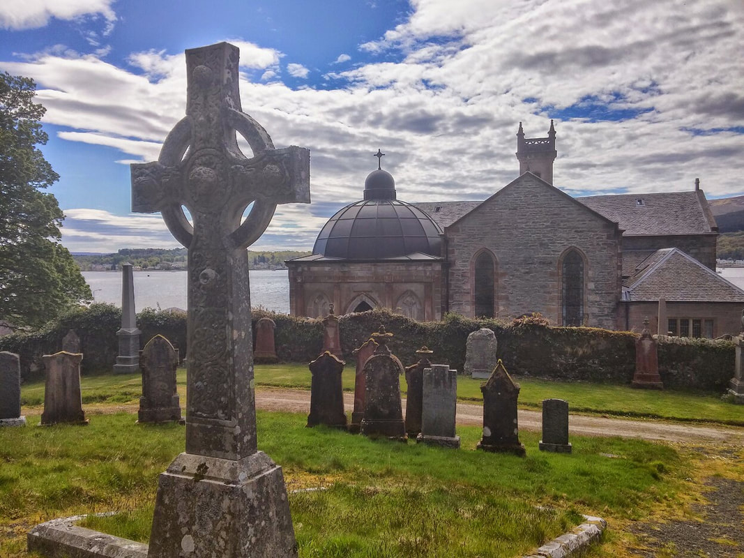 A stone church and graveyard with a stone cross in the foreground